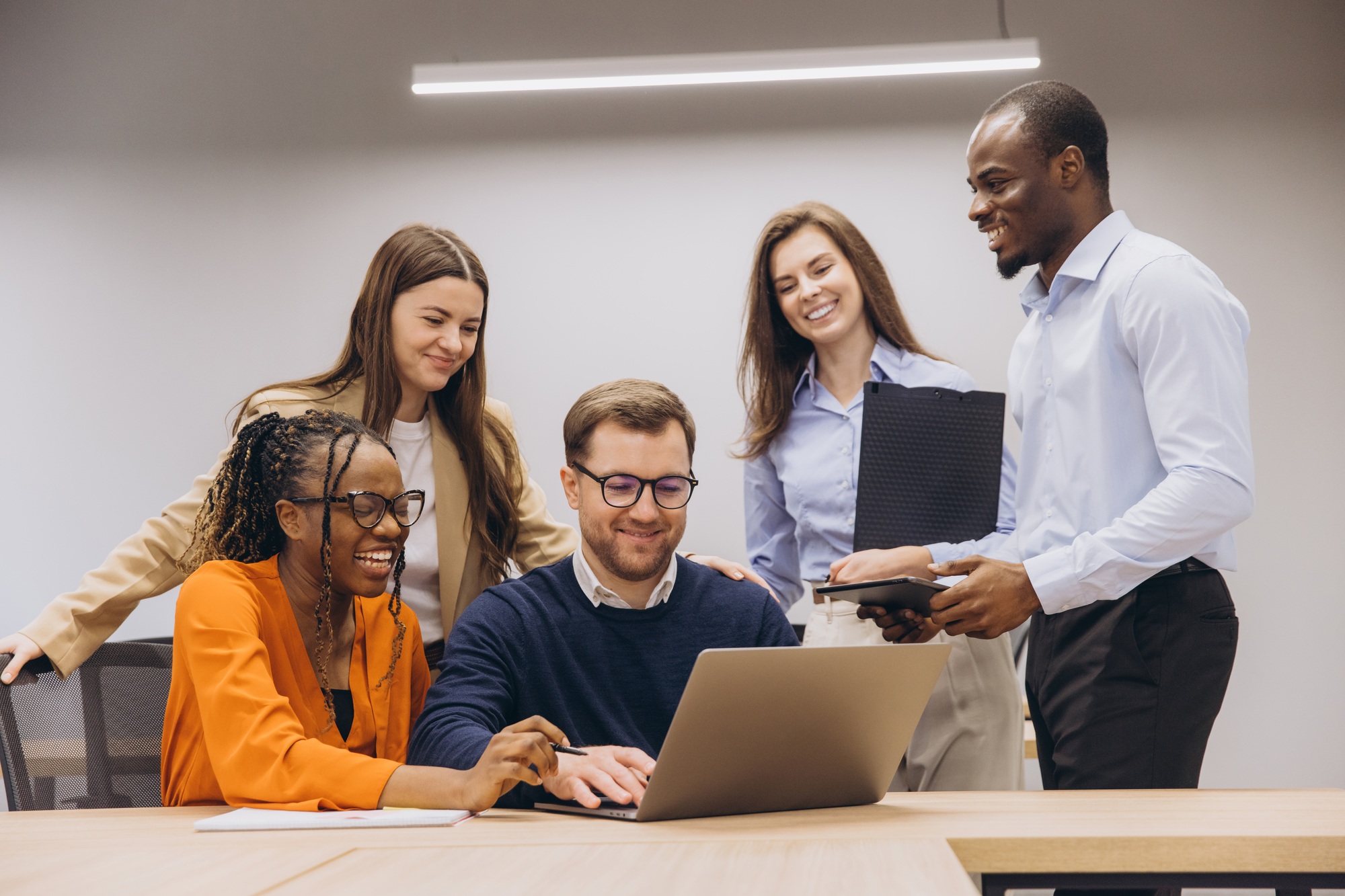Professional team collaborating around laptop, displaying cultural diversity and teamwork in office